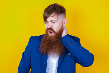 red haired man wearing blue suit over yellow studio background Suffering of neck ache injury, touching neck with hand, muscular pain