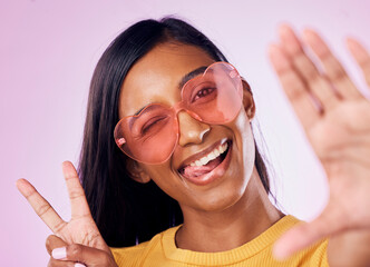 Selfie, peace and indian woman in studio with heart sunglasses, cheerful or fun on purple background. Portrait, v sign and girl gen z style fashion influencer smile for profile picture or blog post