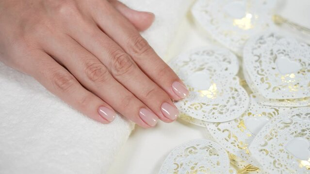 Close up top view 4k video footage of two beautiful manicured female hands with professionally painted in light pink color short fingernails. Arms isolated on white towel whith white hearts decor