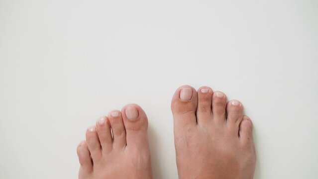 First person top view 4k stock video footage of two female pedicured feet isolated on white empty background with copyspace. Female toenails painted with pink polish