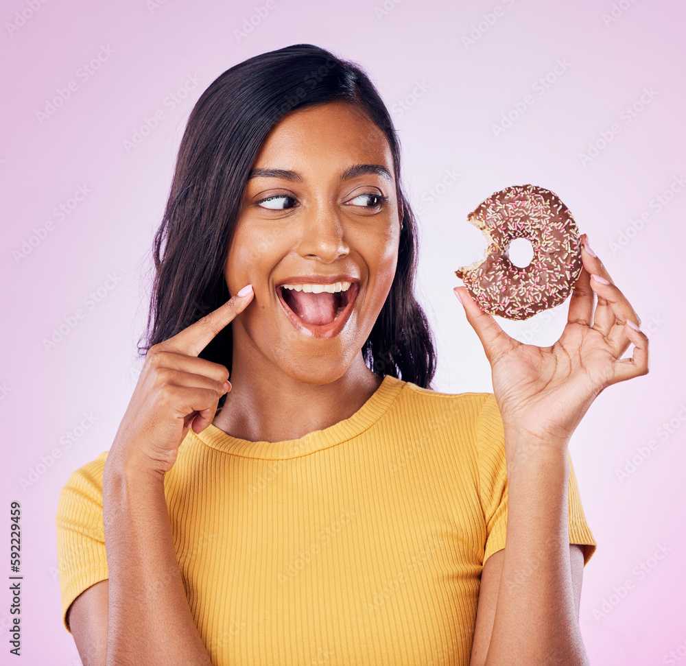 Wall mural Donut, dessert and bite with woman in studio for diet, snack and happiness. Sugar, food and smile with female eating sweets treat isolated on pink background for nutrition, excited and craving mockup