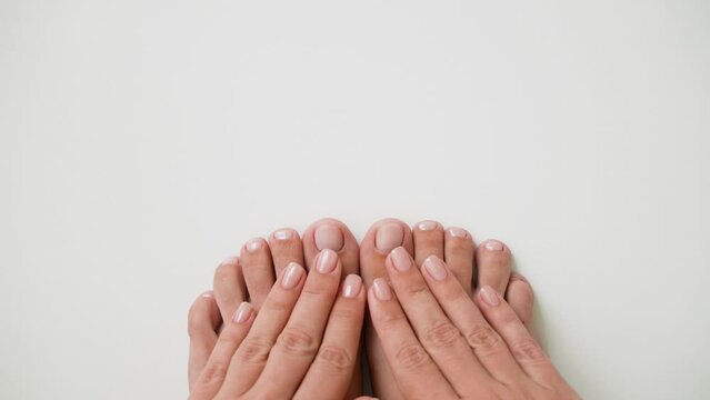 First person top view 4k stock video footage of two female pedicured feet and manicured hands isolated on white empty background with copyspace. Female toenails, fingernails painted with pink lacquer