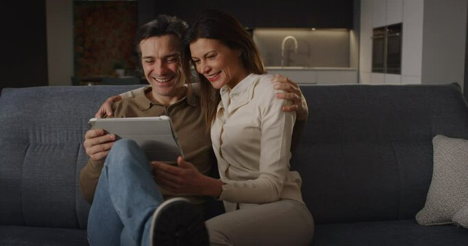Portrait of Couple Using Digital Tablet While Sitting in the Living Room at Home. Husband and Wife Doing Online Shopping to Renovate the House, Browsing the Internet to Compare Sales