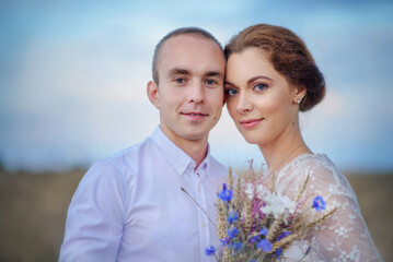 Love story. Wedding day. Newlyweds. Boho style wedding. Bride and groom.A beautiful girl and a guy in a wheat field. Bride with a bouquet of wild flowers.Tenderness.Love.Summer day. Happiness.Portrait
