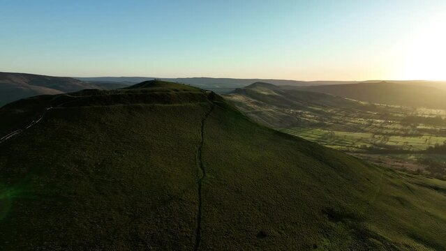 Wide aerial orbit of Mam Tor and the Great Ridge at sunrise in the Peak District, UK with silhouettes of people enjoying the view from the trig point.