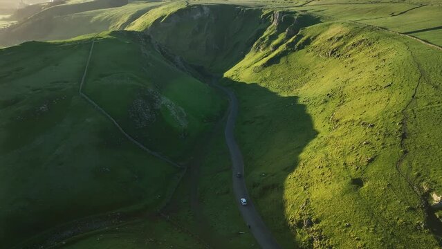 Aerial pull back tilt up reveal of cars using the Winatts Pass in the Peak District, UK to reveal the landscape and dramatic sunrise.
