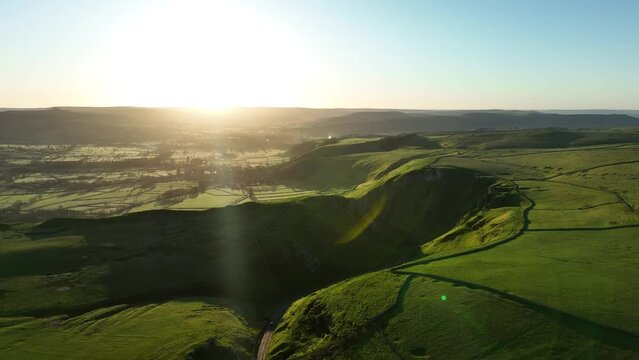 Aerial pull back shot from the Winatts Pass in the Peak District, UK framing the sunrise on the horizon and surrounding dales and peaks.