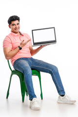 Young indian man sitting on chair and showing laptop screen.