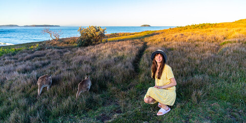A beautiful girl in a yellow dress enjoys a close encounter with adorable eastern grey kangaroos in...