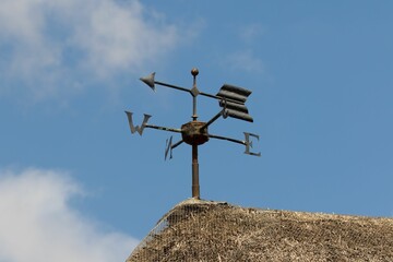 Vintage arrow weather vane with North, East, South and West letters on thatched roof