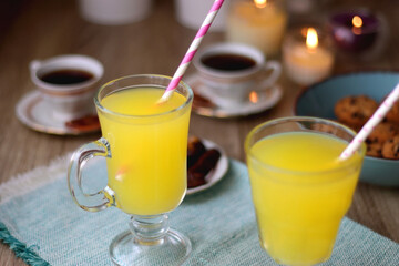 Plate of chocolate pralines, bowl of cookies, cups of tea, glasses of juice and lit candles on the table. Selective focus.