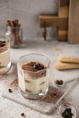Traditional Italian coffee dessert Tiramisu made from mascarpone cheese and savoiardi cookies or biscuit in a cup on a concrete background.