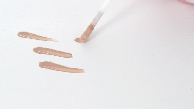 Smearing foundation tones on white background. Brown cream texture close-up, using brush. Makeup and beauty products concept, cosmetics, eyeshadow palette, bronzer or concealer.