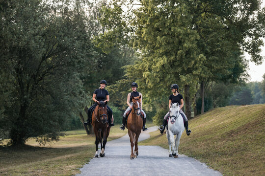 Three female riders riding horses along the trail by the river. Recreation and leisure activity concepts.