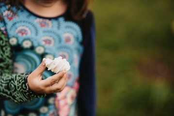 Kid holding a white cream in her hand in a garden in a blurred background
