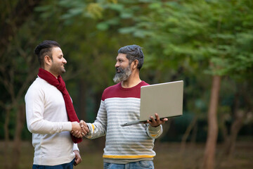 Two indian man using laptop at park.