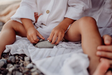 A small child, a girl in a white dress, plays with sea stones that she holds in her hands