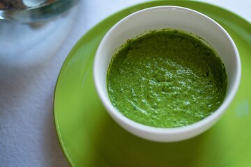Spinach and pea cream soup served in green bowl, close-up