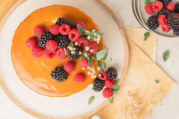 Delicious chocolate cake topped with mascarpone cream and salted caramel. Decorated with red fruits. Light background