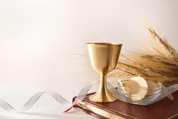 Cup and hosts on bible with ribbon and wheat ears