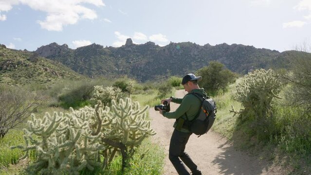 Caucasian man stops to take photos of a cactus on a hike in the desert mountain landscape of Arizona in the summer
