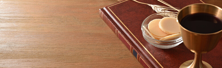 Hosts in container and cup on bible in wooden table