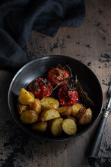 Roasted potatoes and tomatoes in a black plate. Rustic food.