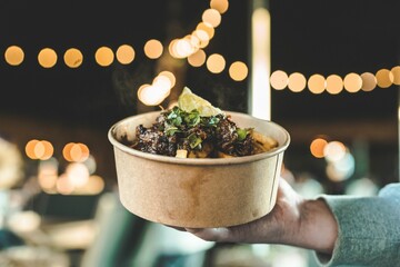 Closeup shot of a person holding a paper bowl with street food