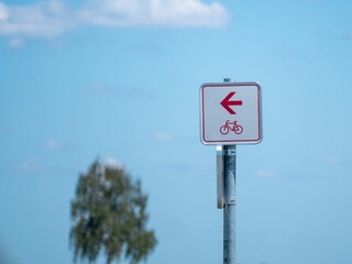 Signpost with a red arrow pointing toward a bike path under a bright blue sky