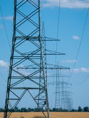 Vertical shot of a line of transmission towers in a field in the countryside under a cloudy sky