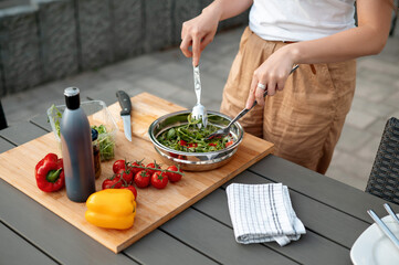 Close up view of the young woman hands mixing salad and cooking in the outdoor kitchen