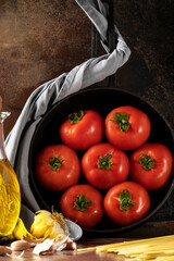Fresh tomatoes in the pan and extra virgin olive oil on the dark background
