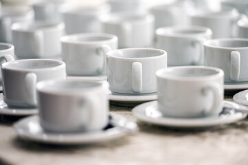 a lot of rows of pure white cups with plates for coffee or tea break