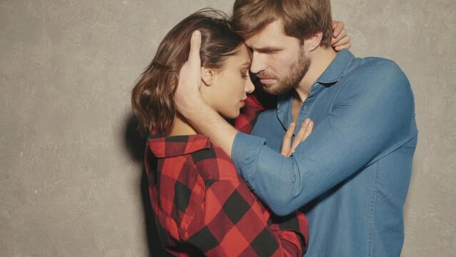 Hot beautiful woman and her handsome boyfriend. Models posing near grey wall in jeans clothes. Young passionate couple hugging before having sex.  Sensual pair getting closer for kiss. Lover couple
