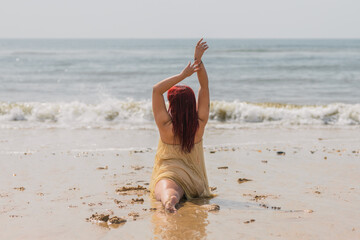 Back view of woman with red hair and dress dancing lying on the shore of the beach