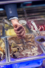 Man's hand picking up a portion of chocolate ice cream in a showcase