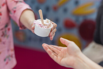 close-up holds out a hand with ice cream. Give a paper cup of ice cream.