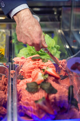 man's hand picks up ice cream in a showcase