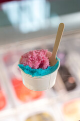 pink and blue ice cream in a paper cup with a wooden spoon.