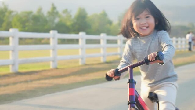 Happy cheerful little asian girl balancing bike running along the outdoor road, summer outdoor activity, kids playground, enjoy ride a bike, kids playtime for good emotion, child growth hormones, 