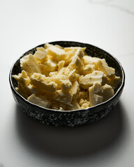 Broken white chocolate in a black ceramic bowl. The main ingredient for making blondies. White marble backgorund