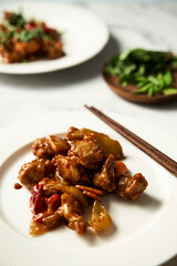 Chicken Manchurian on white plate with chopsticks. White marble background. Sweet and sour Chinese chicken recipe 