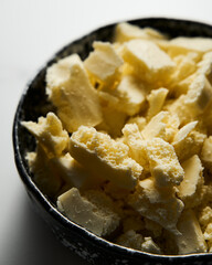 Broken white chocolate in a black ceramic bowl. The main ingredient for making blondies. White marble background. Close up.