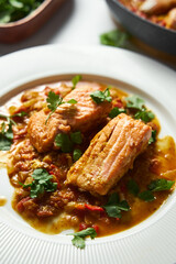 Indian red salmon curry with tomatoes. Asian Cuisine. Tomato-infused Red Salmon Curry and Fried Vegetables with Green Cilantro. Close up. Vertical photo 