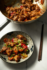 Chicken Manchurian in plate near wok where chicken was fried and cooked with sauce. Top view