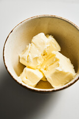 Unsalted butter cubes in white bowl on white marble background. The oil is at room temperature, soft and fluffy. 