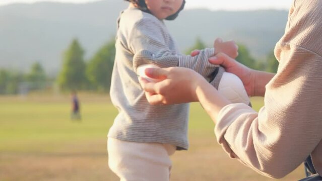 Affectionate father helping little black-haired asian girl wearing safety elbow pad before playing at outdoor grass field park, putting on elbow pads, taking care of child. Active Activity and Kid
