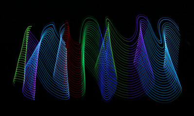 Abstract waves of bright and vibrant multi colored LED light trails on a black background