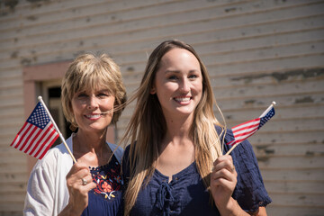 This image shows a mother and daughter posing together while holding American flags. - obrazy, fototapety, plakaty