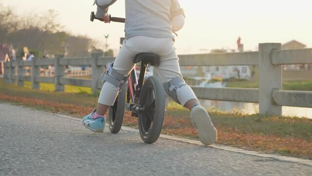Low angle shot of child ride standing bike with no parents around, riding along the river with beautiful golden sunset on the background, young age learning from experiences, growing path, girl bike